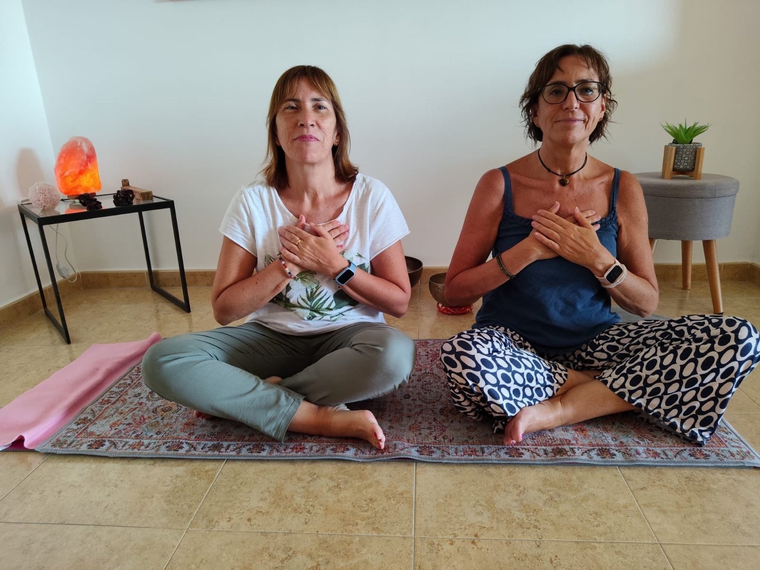 Maribel y Sonia sentadas en meditación, con las manos sobre el pecho.